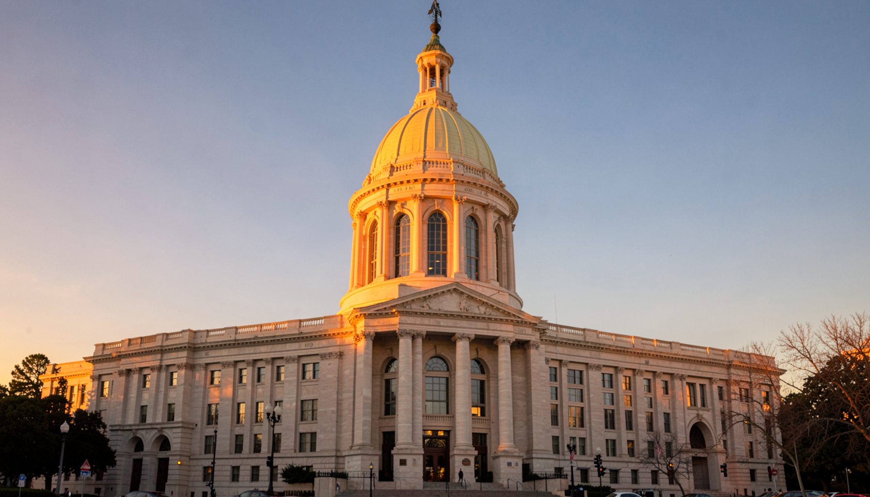 Warm golden-hour photograph of the Texas State Capitol building in downtown Austin, with soft amber light washing over the limestone facade and a clear blue sky above, conveying authority and civic pride.